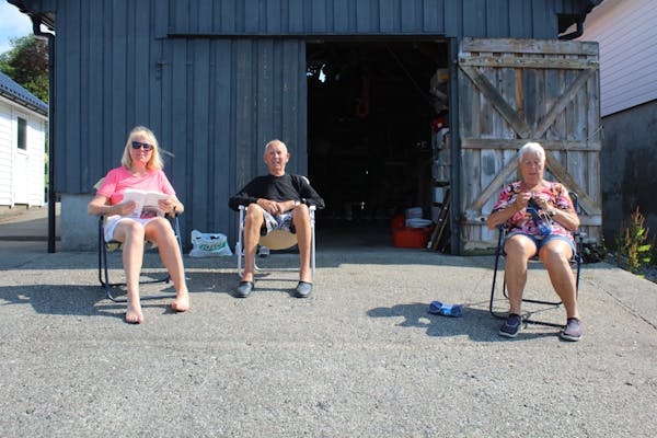 Wenche Nesse Gjesdal (55), Kåre Nesse (88) og Kirsten Nesse (87) nyt sola utanføre naustet deira i Vikebygd.